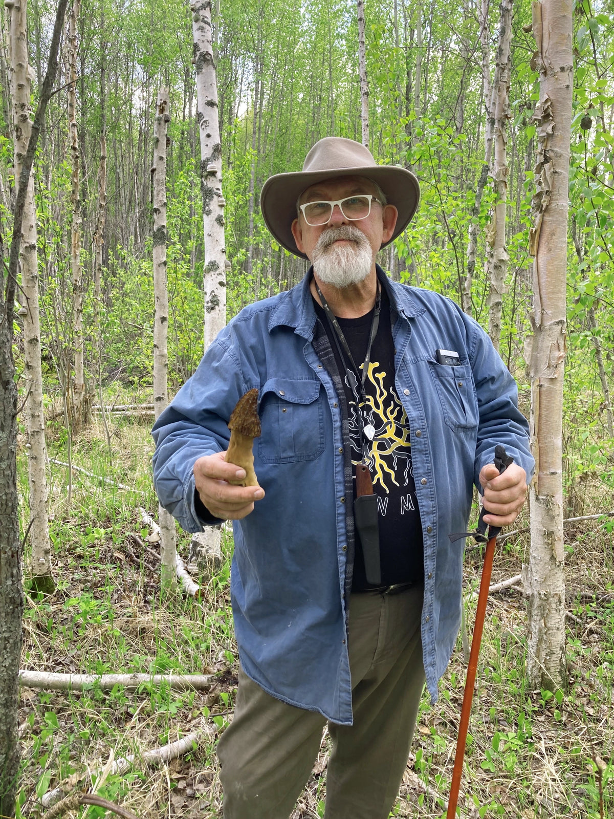 Martin Osis in a forest holding a morel and walking stick